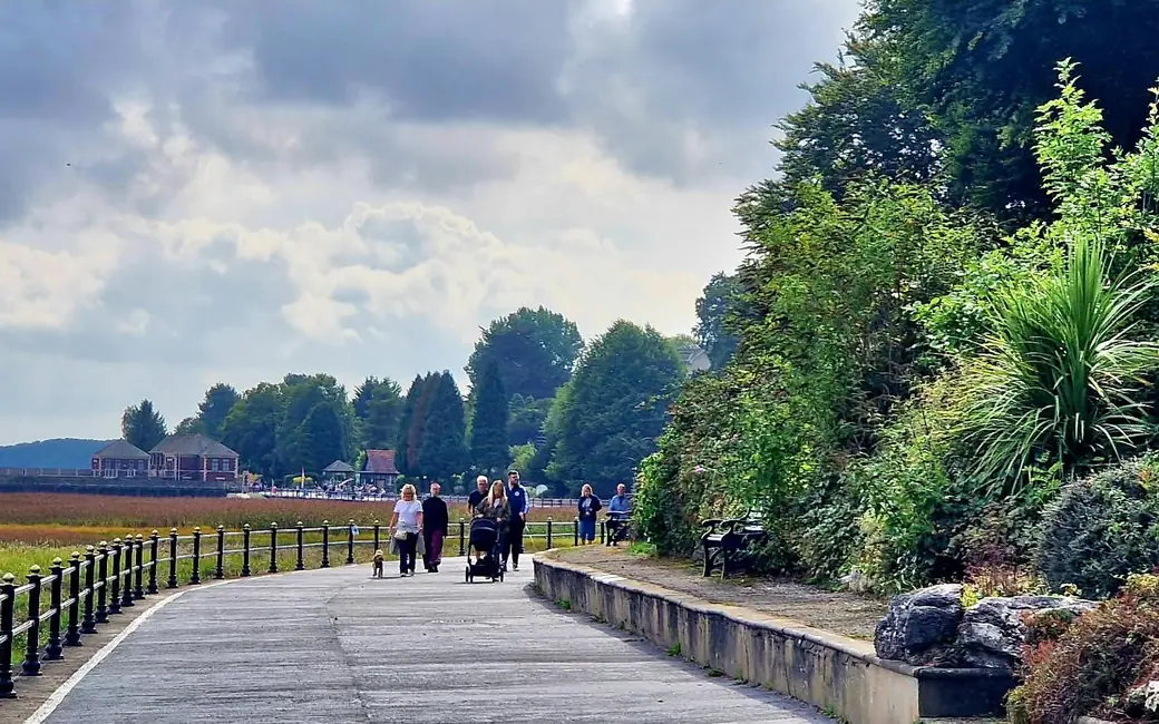 Walkers on the railed Edwardian promenade at Grange-over-Sands, the salt marsh of Morecambe Bay stretching away on one side